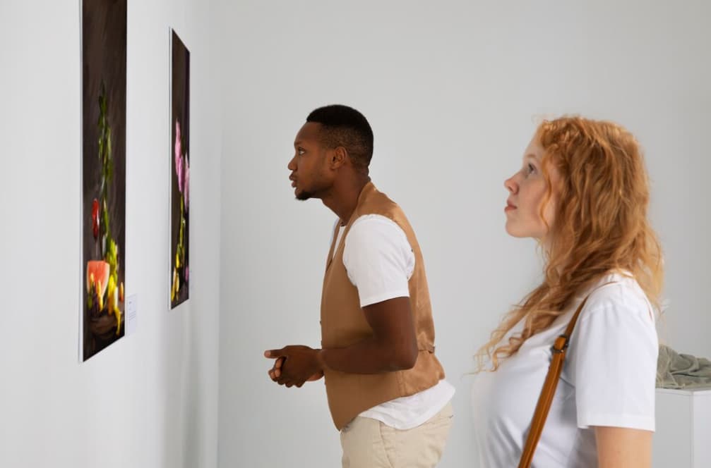 Two people attentively observe paintings in an art gallery