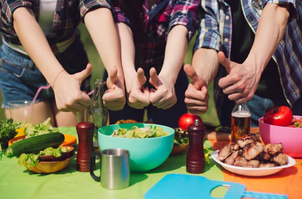 People sitting outdoors giving thumbs up over a picnic table