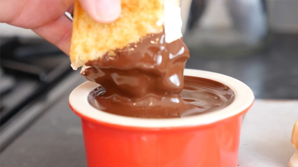 A hand dipping a cracker into a bowl of chocolate