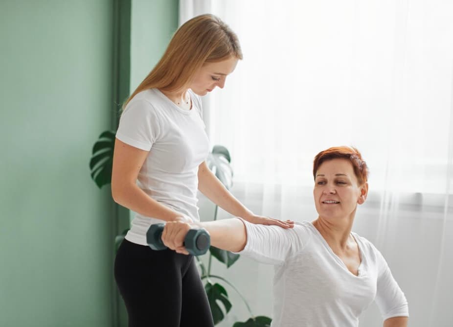 A physiotherapist helping an older woman exercise with dumbbells