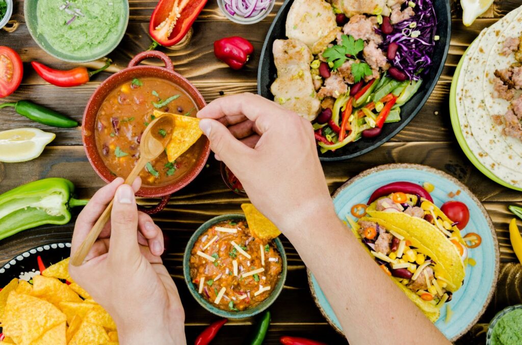 Top view of  hand holding spoon and nacho near mexican food