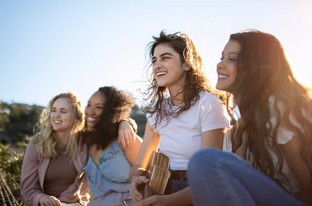 women sitting on the beach, smiling and looking at the side under the sunlight