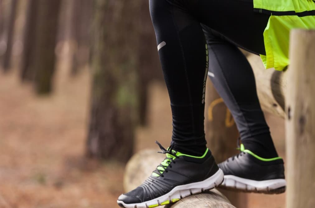 Legs crossed wearing black leggings and black sneakers with green accents
